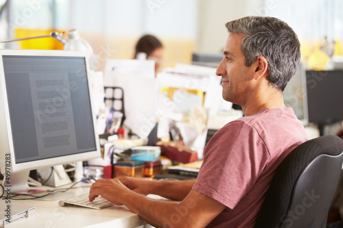 Photo: Man Working At Desk In Busy Creative Office Man Working At Desk In Busy Creative Office