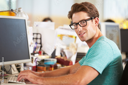 Photo: Man Working At Desk In Busy Creative Office Man Working At Desk In Busy Creative Office
