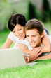Couple lying on the green grass with the silver laptop