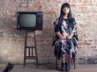 woman and an old television in front of a brick wall.