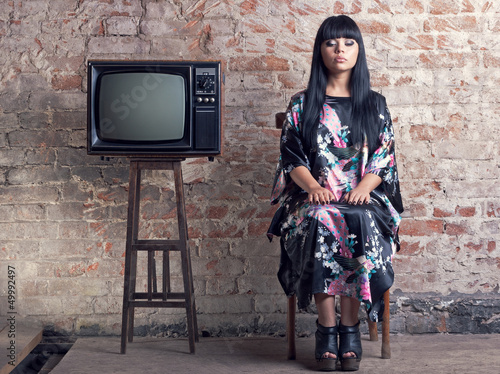 Photo: woman and an old television in front of a brick wall. woman and an old television in front of a brick wall.