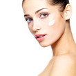 Beautiful face of young woman with cosmetic cream on a cheek.