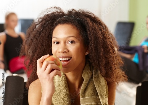 Photo: Attractive ethnic girl eating apple at gym Attractive ethnic girl eating apple at gym