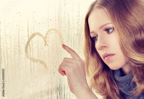 Photo: sad girl draws a heart on the window in the rain sad girl draws a heart on the window in the rain