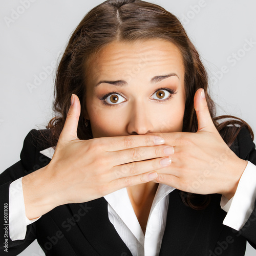 Photo: Business woman covering mouth, over gray Business woman covering mouth, over gray