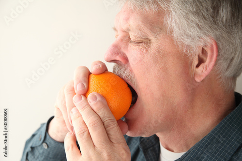 Photo: older man bites into orange to start the peeling process older man bites into orange to start the peeling process