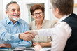 Foto: senior couple smiling while shaking hand with financial advisor senior couple smiling while shaking hand with financial advisor