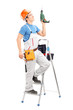 A young worker on a ladder holding a driller