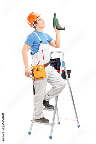 Photo: A young worker on a ladder holding a driller A young worker on a ladder holding a driller