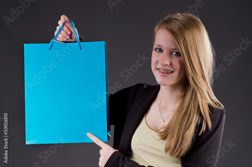 Photo: Blondes Mädchen zeigt auf blauen Shopping Bag Blondes Mädchen zeigt auf blauen Shopping Bag