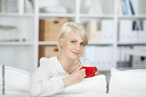 Photo: junge frau trinkt eine tasse kaffee auf dem sofa junge frau trinkt eine tasse kaffee auf dem sofa