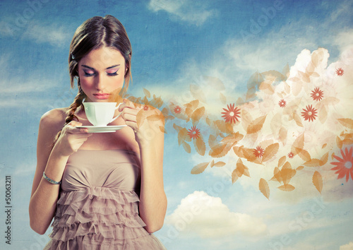 Photo: Beautiful young woman holding a cup of tea over a sky background Beautiful young woman holding a cup of tea over a sky background