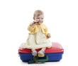 little baby girl seated on a red and blue suitcas