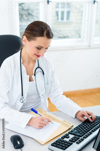 Photo: doctor at desk in clinic writing a file or dossier doctor at desk in clinic writing a file or dossier