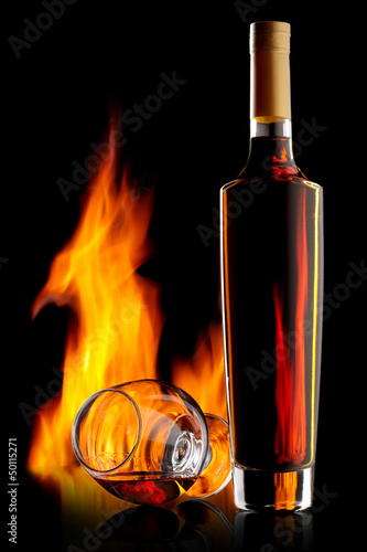 Photo: Bottle and glass of cognac over dark background with flame Bottle and glass of cognac over dark background with flame