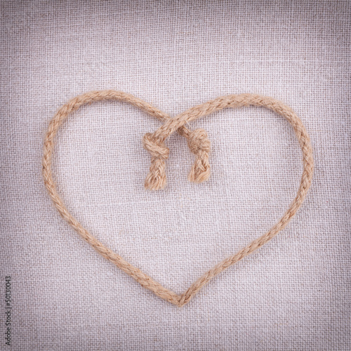 Photo: A love heart made of string on fabric vintage background A love heart made of string on fabric vintage background