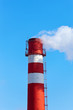 Foto: Red and white factory chimney with smoke against blue sky Red and white factory chimney with smoke against blue sky