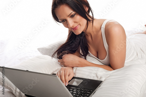 Photo: Smiling woman using a laptop in bed Smiling woman using a laptop in bed