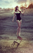 beautiful girl balances on back of chair outdoors.