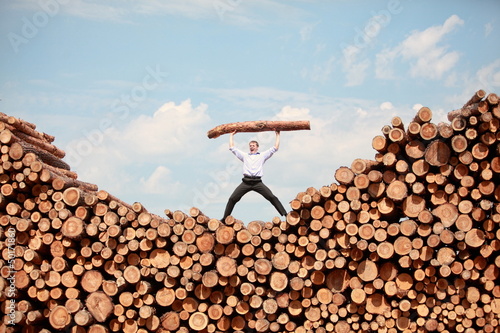 Photo: man on top of large pile of logs, shouting, lifting heavy log man on top of large pile of logs, shouting, lifting heavy log