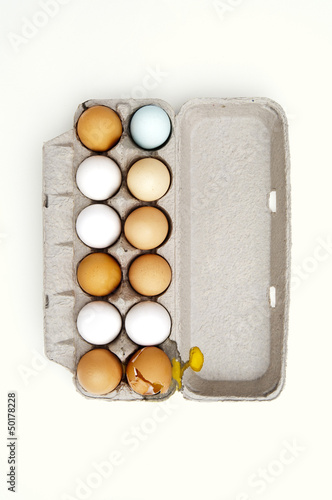 Photo: Colored eggs and one broken egg in carton Colored eggs and one broken egg in carton