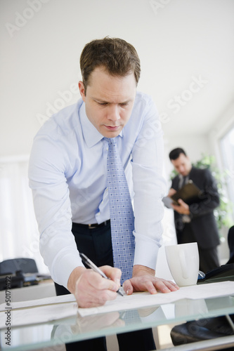 Photo: Caucasian businessman leaning on desk and writing Caucasian businessman leaning on desk and writing