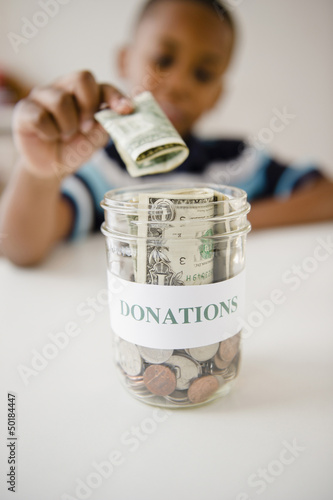Photo: Black boy putting money into donations jar Black boy putting money into donations jar