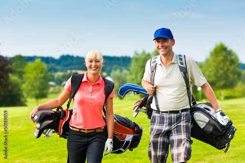 Photo: Young sportive couple playing golf on a course Young sportive couple playing golf on a course
