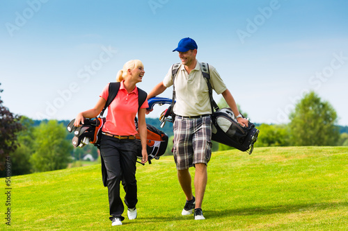 Photo: Young sportive couple playing golf on a course Young sportive couple playing golf on a course