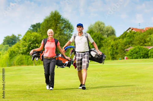 Photo: Young sportive couple playing golf on a course Young sportive couple playing golf on a course