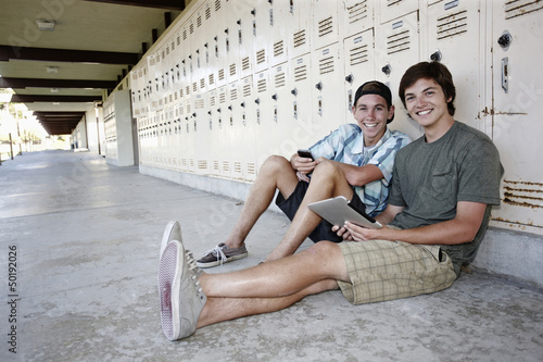 Photo: School friends leaning on lockers using digital tablet School friends leaning on lockers using digital tablet