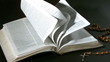 Bible pages turning in the wind beside rosary beads