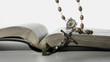Rosary beads falling onto open bible on close up