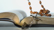 Rosary beads falling on open bible on white background close up