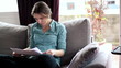 Young woman reading documents on sofa in home
