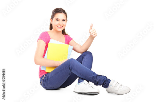 Photo: Young female student sitting on floor and giving thumb up Young female student sitting on floor and giving thumb up
