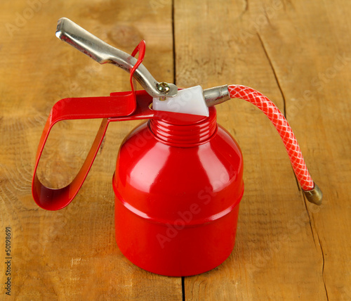 Photo: Red oil can, on wooden background Red oil can, on wooden background