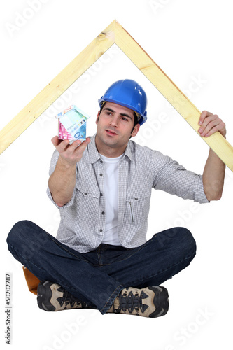 Photo: A carpenter presenting a miniature house made of euro bills. A carpenter presenting a miniature house made of euro bills.