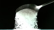 Spoon pouring white sugar on black background
