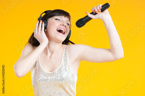 Photo: Expressive woman singing with a mike over yellow background Expressive woman singing with a mike over yellow background
