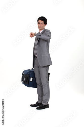 Photo: Businessman with suitcase looking at wrist watch Businessman with suitcase looking at wrist watch