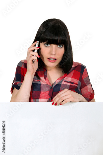 Photo: Woman on a cellphone with a board left blank for your message Woman on a cellphone with a board left blank for your message