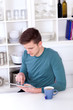 Photo: young man sitting with a tablet pc and tea cup in the kitchen young man sitting with a tablet pc and tea cup in the kitchen