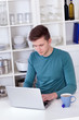 Photo: young man sitting with a laptop and tea cup in the kitchen young man sitting with a laptop and tea cup in the kitchen