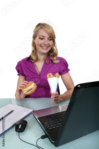 Photo: A businesswoman having junk food in her office. A businesswoman having junk food in her office.