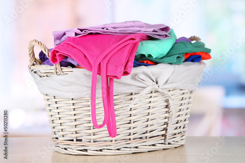 Photo: Clothes in wooden basket on table in room Clothes in wooden basket on table in room