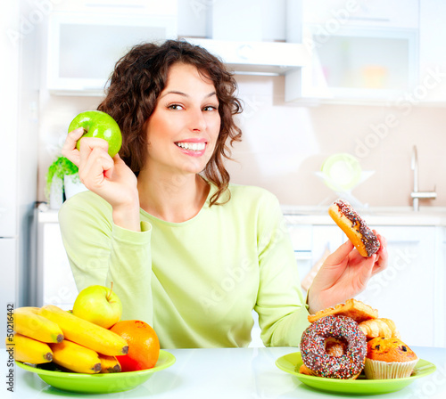 Photo: Dieting concept. Young Woman choosing between Fruits and Sweets Dieting concept. Young Woman choosing between Fruits and Sweets