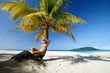 Dreaming woman sitting on the beach under a palm tree on a beaut