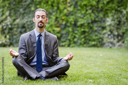 Photo: Young businessman meditating in the garden Young businessman meditating in the garden