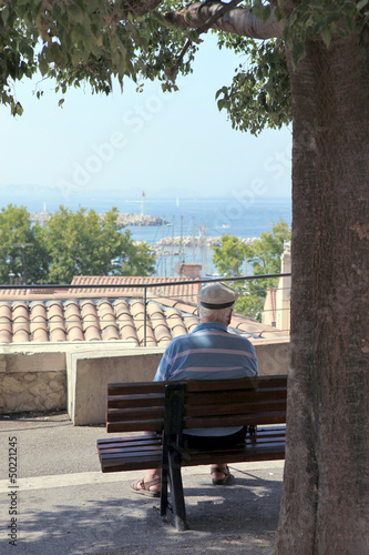 Photo: Old man sat on a bench by the coast Old man sat on a bench by the coast